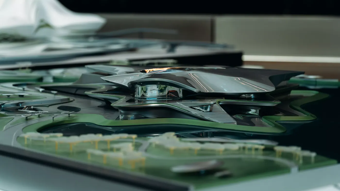Close-up of a sleek architectural model with a metallic building form set among a green landscape