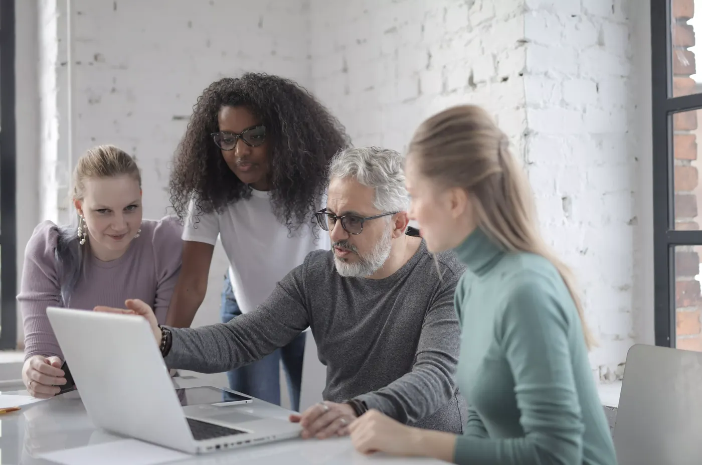 Four colleagues gathered around a laptop, one pointing at the screen while explaining a business project