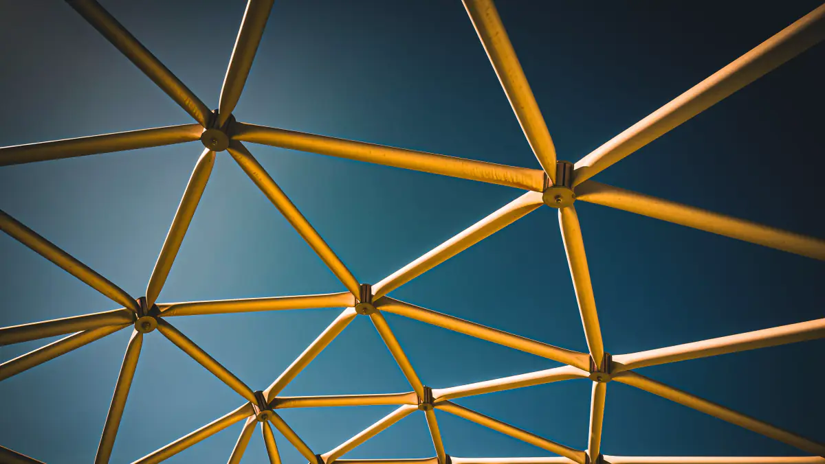 Interlocking triangular struts of a geometric dome structure, seen from below against a blue sky