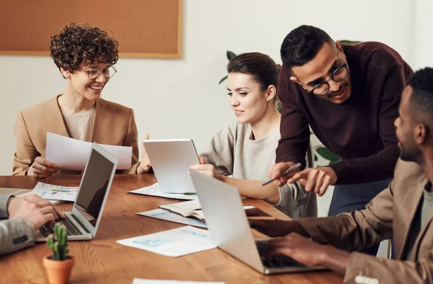 A small group of colleagues at a wooden desk reviewing documents and a tablet together